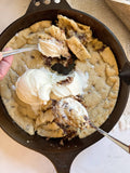 Large cookie in a skillet with ice cream being scooped onto it